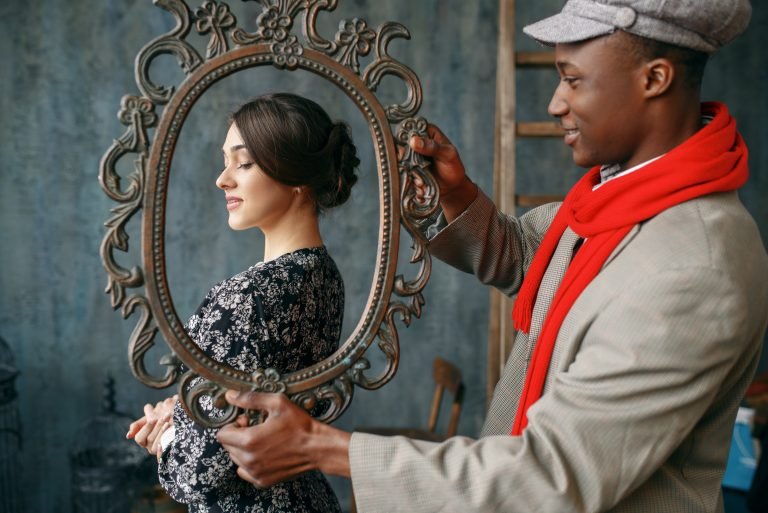 A man holding a frame in front of a woman. Simulating a protrait.