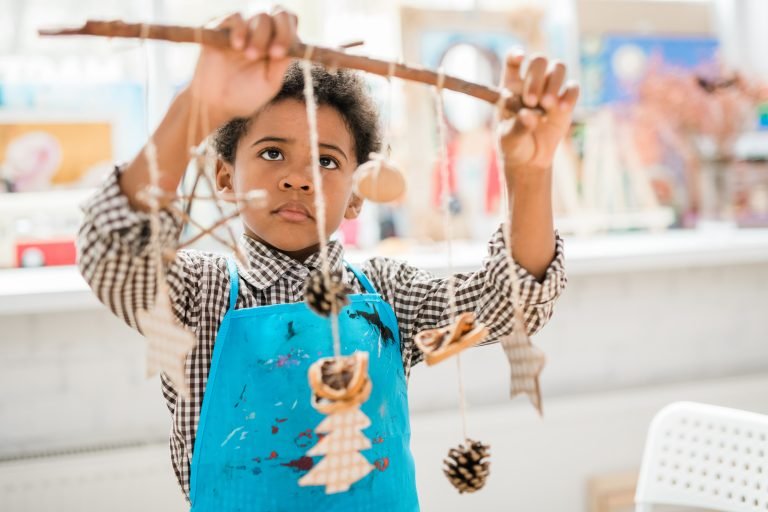 Open-Ended play. A boy in blue apron looking at stick with group of loose parts.